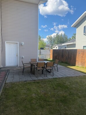 Eine Terrasse mit Tisch und Stühlen, eine weiße Tür und ein Holzzaun.