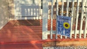Ein Hauseingang mit weißer Tür, einem Willkommen-Schild und einer Veranda mit rotem Boden.