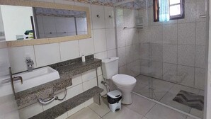 A bathroom with a marble wall, a sink, a toilet, and a shower area. - Pousada Nascimentos (Bertioga)
