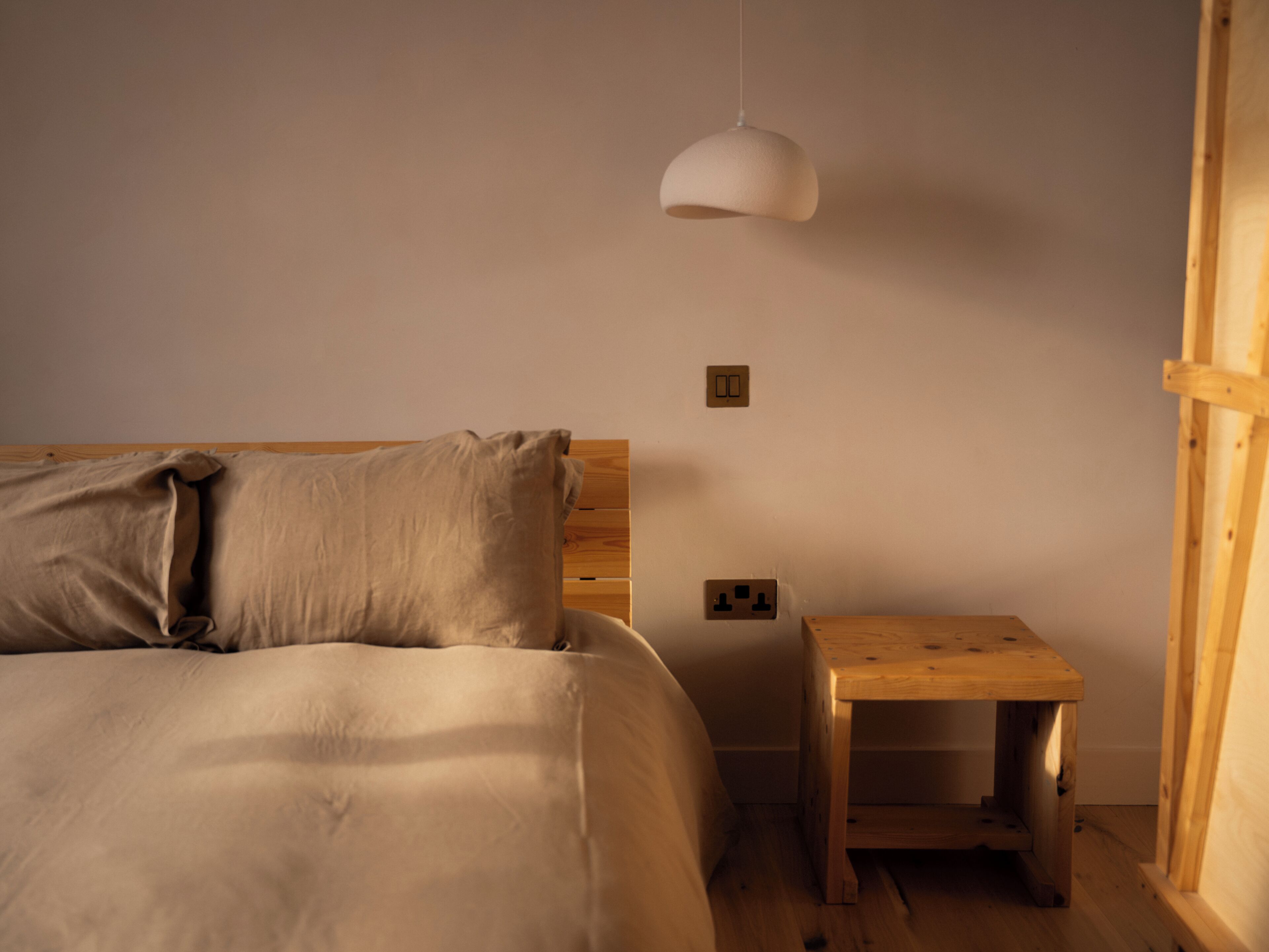 A bedroom with a bed, a bedside table, a hanging light fixture, and electrical outlets on the wall.