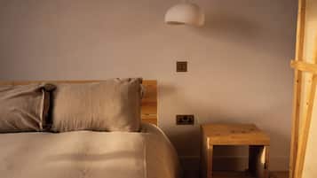 A bedroom with a bed, a bedside table, a hanging light fixture, and electrical outlets on the wall.