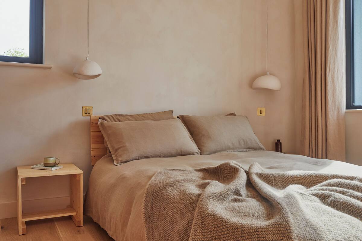 A bedroom with a bed, two bedside tables, a lamp, and a window with curtains.