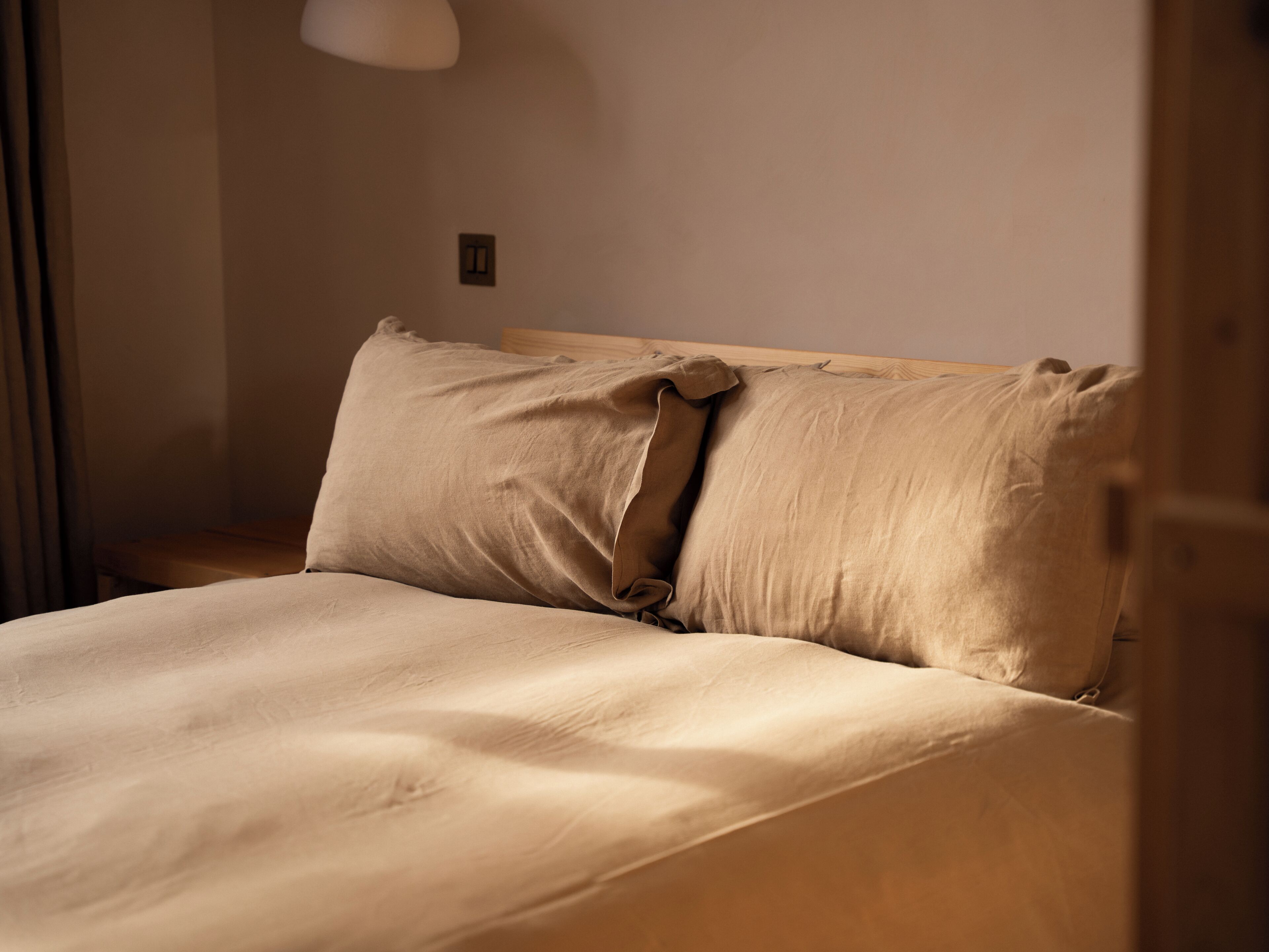 Una cama con cabecera de madera, una almohada y una mesita de noche con una lámpara.