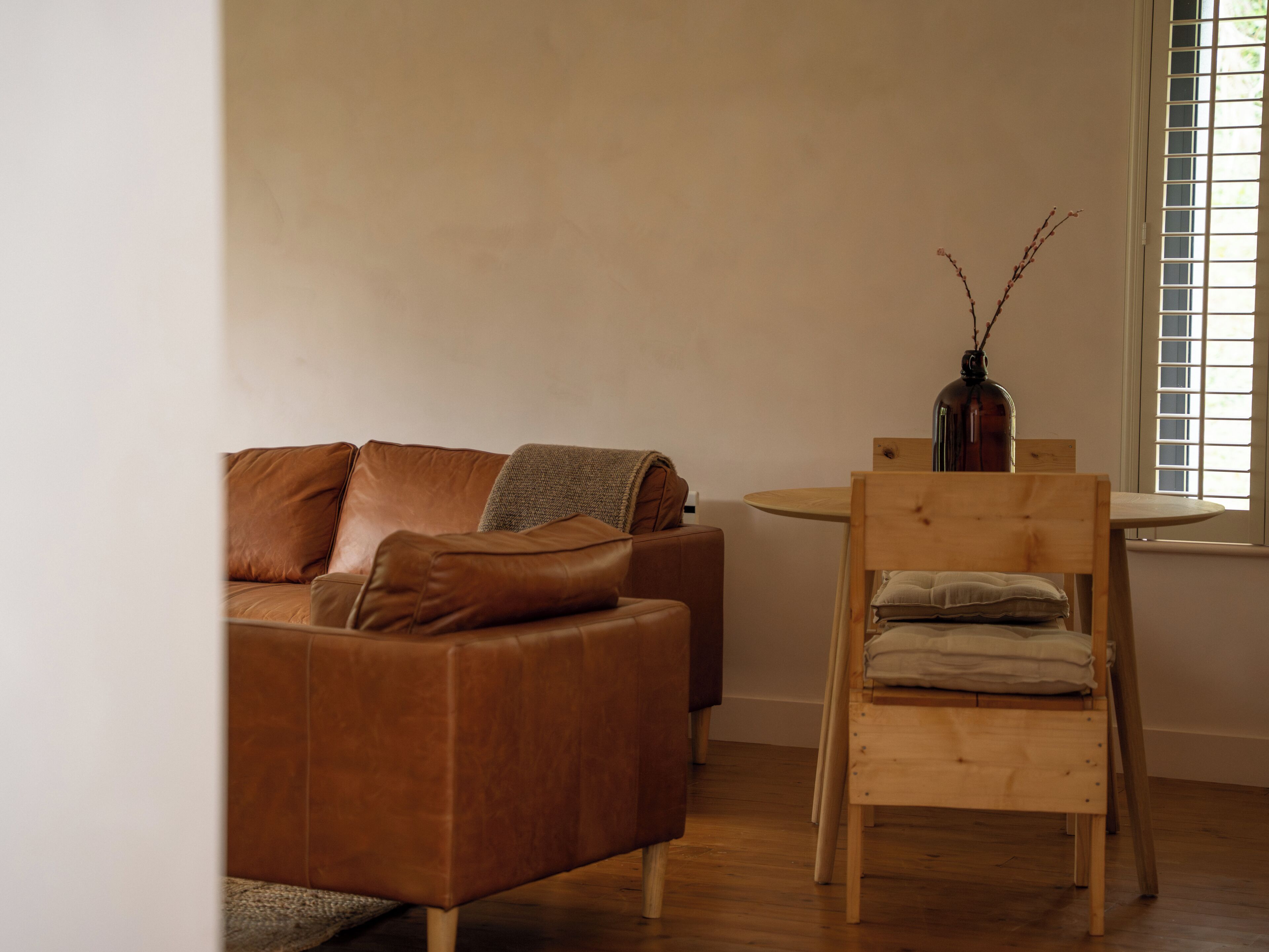 Un salón moderno con un sofá de cuero marrón, una silla de madera y una mesita con un florero.