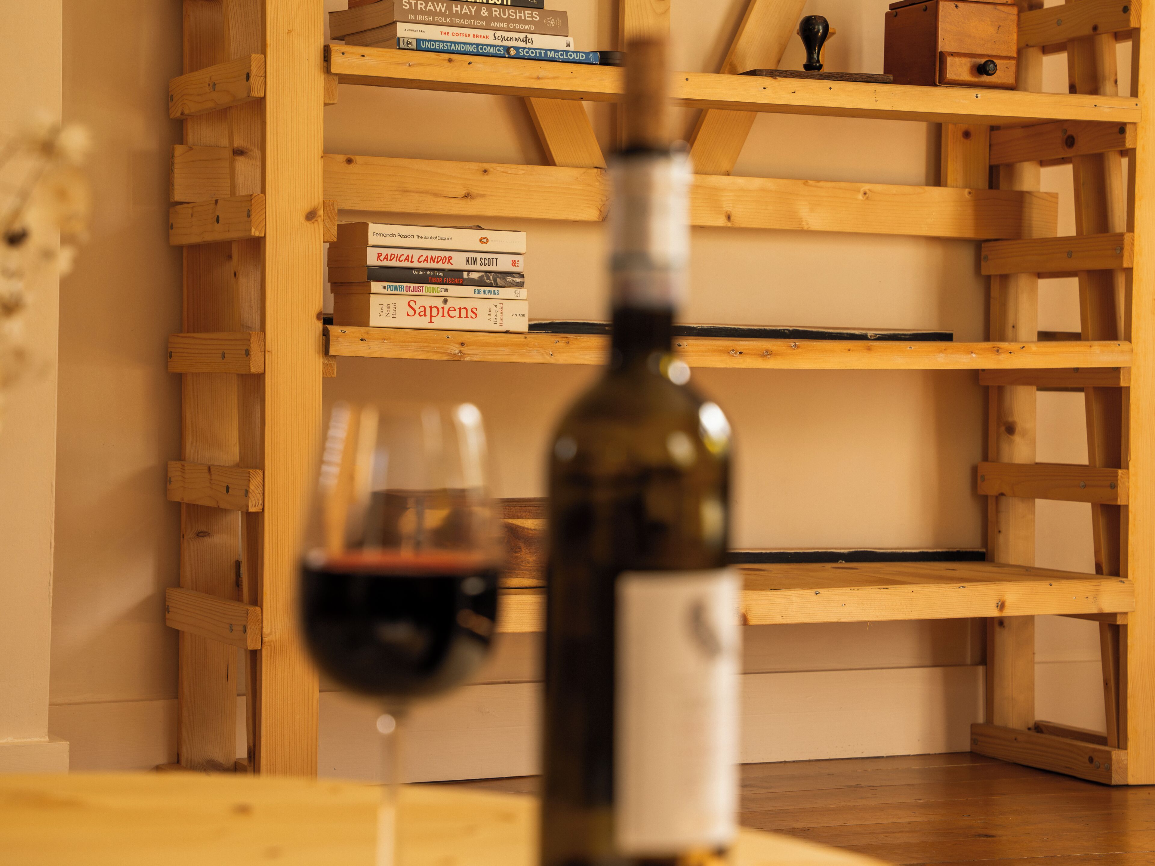 A wooden bookshelf with books and a wine bottle.