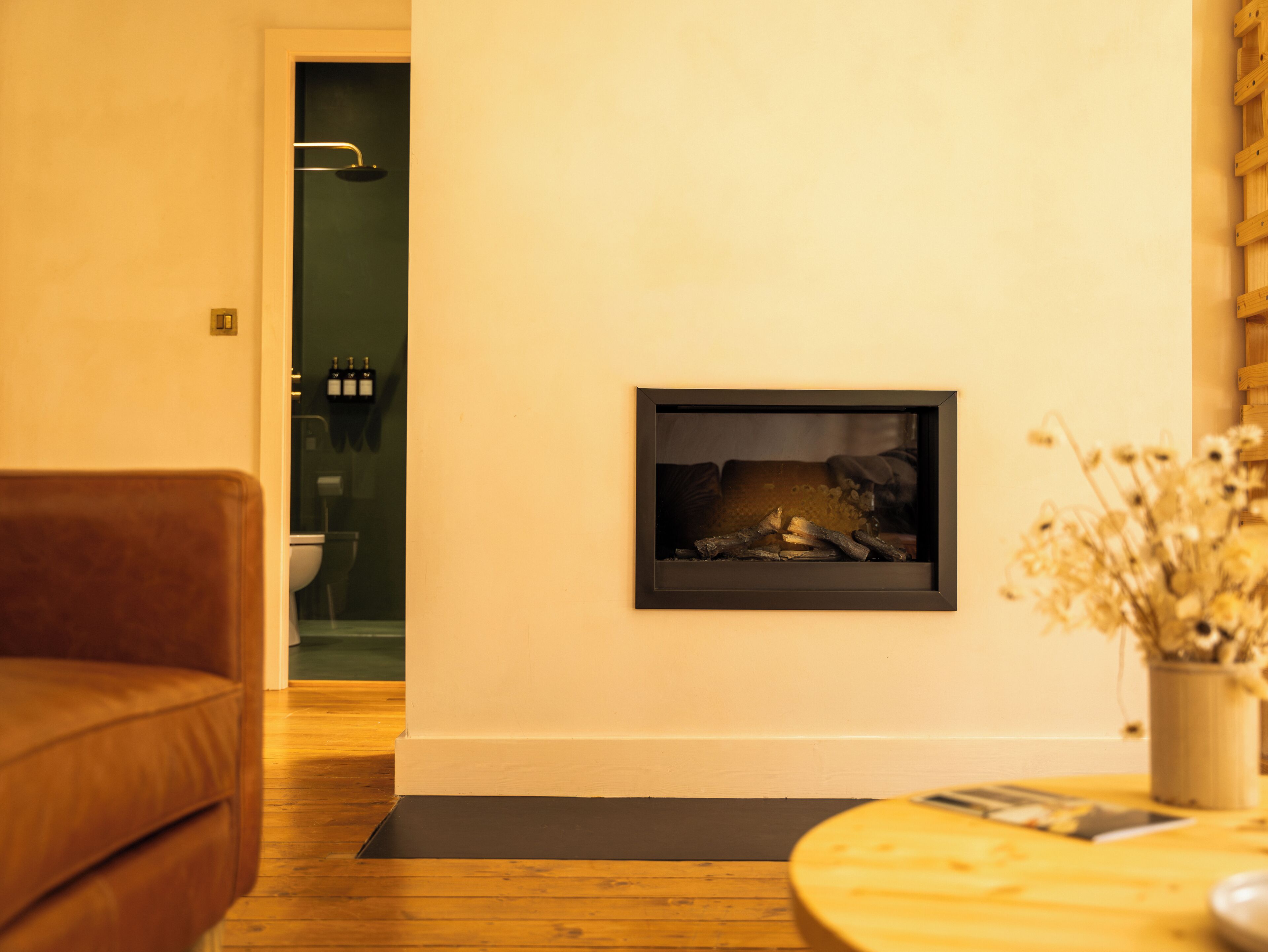 A living room with a fireplace, a brown leather sofa, a wooden floor, and a small round table with a vase of flowers.