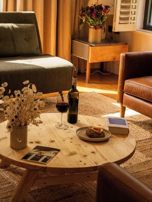 A cozy room with a bed, a wooden coffee table with a bottle, wine glass, and a book, and a leather chair.