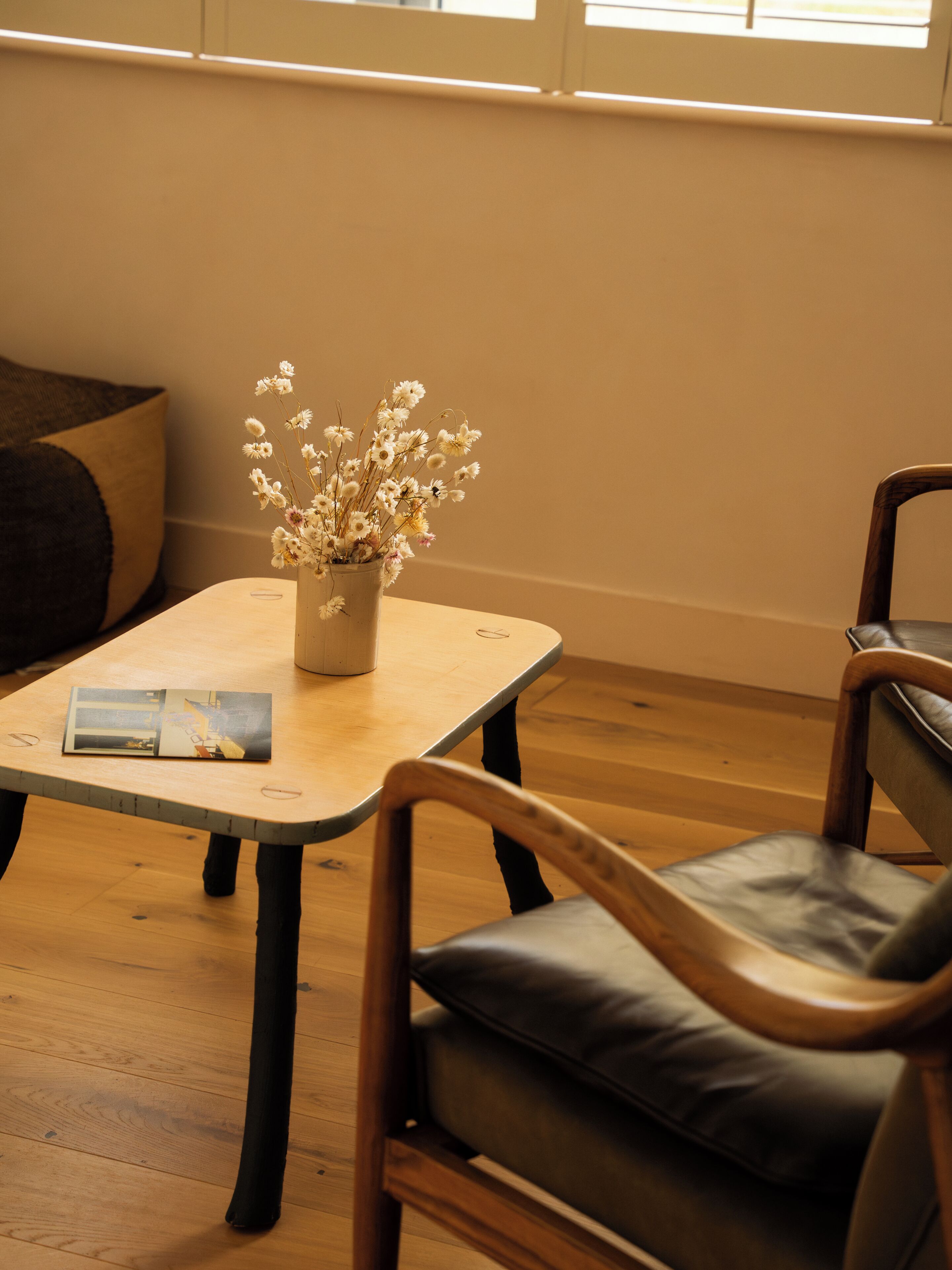 Une pièce avec une table en bois, un vase contenant des fleurs séchées, un magazine et deux chaises.