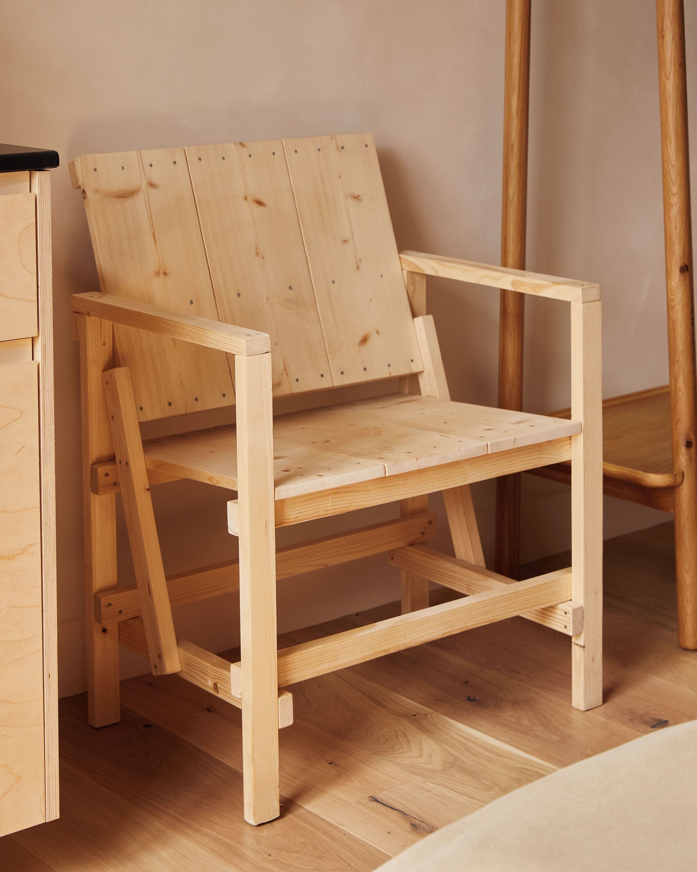 Een houten stoel met een latten rugleuning en een vlakke zitting, staand op een houten vloer.