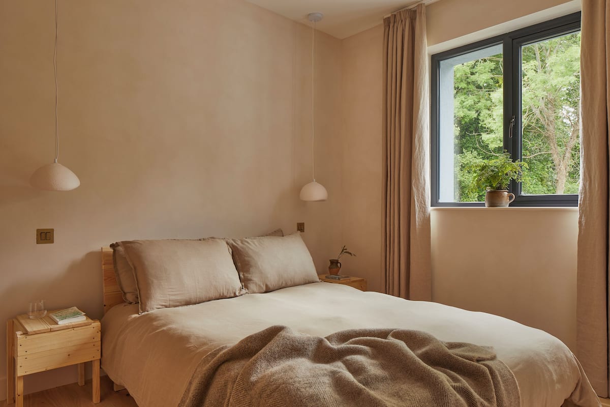 A bedroom with a bed, bedside tables, a window with curtains, and a potted plant.