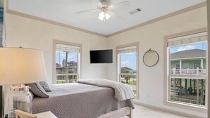 A bedroom with a bed, a TV mounted on the wall, and large windows offering a view of the outside. - This 3 bedroom beach house is the PERFECT space to get “A Wave From It All! "  (Crystal Beach)