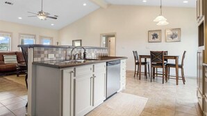A spacious kitchen with a central island, a dining area with wooden chairs, and a ceiling fan. - This 3 bedroom beach house is the PERFECT space to get “A Wave From It All! "  (Crystal Beach)
