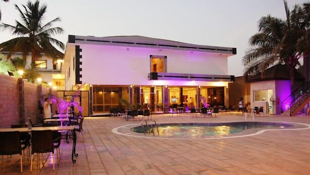Een modern hotel met een zwembad, terras en palmbomen.