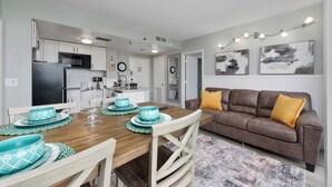 Una cocina moderna con armarios blancos, un refrigerador negro y una zona de comedor con una mesa de madera para cuatro.
