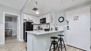 Una cocina moderna con gabinetes blancos, un refrigerador negro, un microondas y un fregadero. Hay dos taburetes negros en la isla.