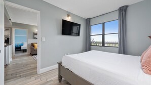 Un dormitorio con una cama, un televisor instalado en la pared y un ventanal con vistas.