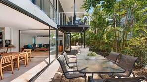 Una casa moderna con un patio acristalado, muebles de exterior y exuberante vegetación tropical.