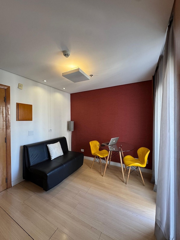 A modern living room with a black sofa, two yellow chairs, a small table with a laptop, and a red accent wall.