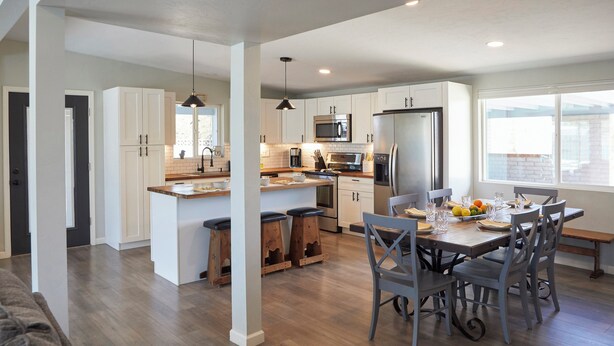 A modern kitchen with white cabinets, a central island, and a dining area with a wooden table and chairs.