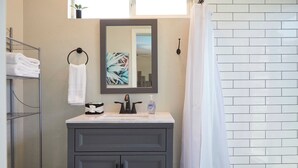 A bathroom with a grey vanity, a white sink, a mirror, a towel rack, and a shower curtain.