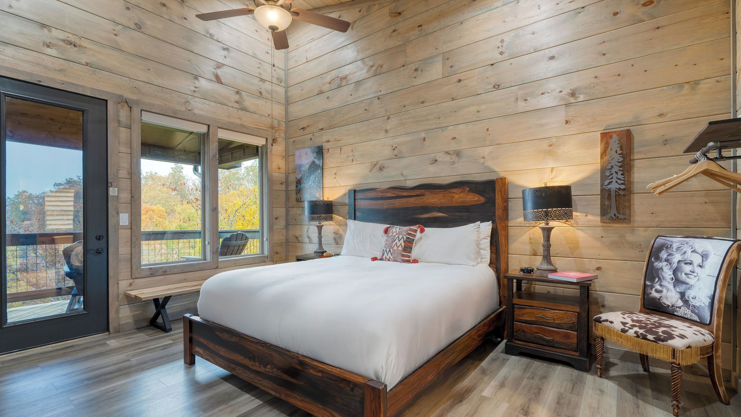 A wooden cabin bedroom with a large bed, two bedside tables, a chair, and a ceiling fan.