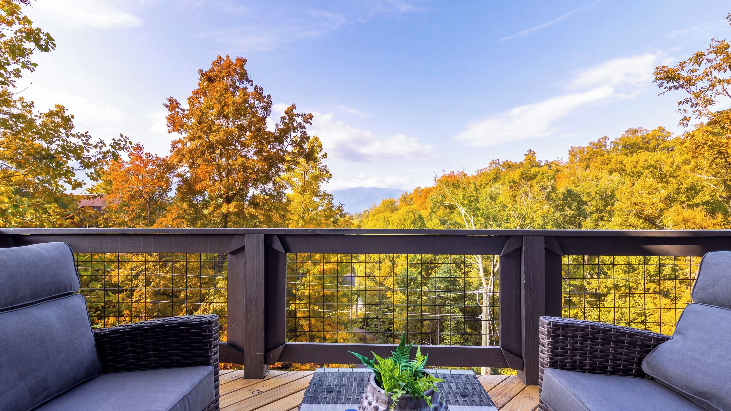 A deck with two grey cushioned chairs and a small table, surrounded by a metal grid railing.
