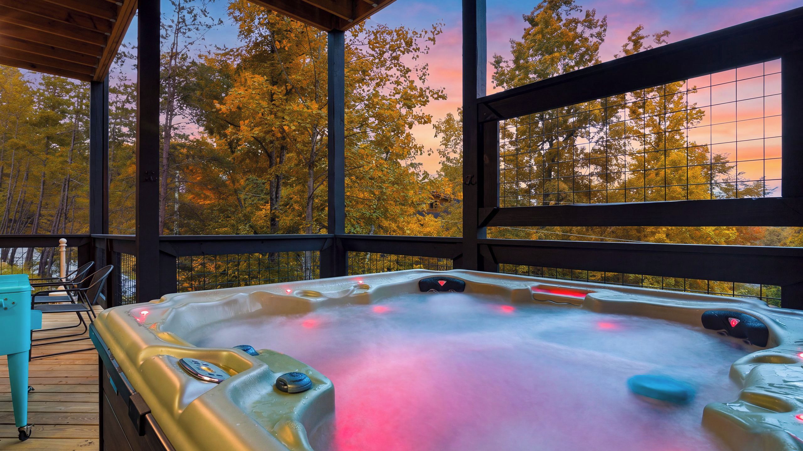 Un bain à remous sur une terrasse en bois, avec vue sur les arbres aux couleurs automnales à travers de grandes fenêtres.