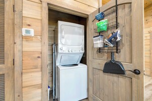 Un área de lavandería compacta con lavadora y secadora, un termostato digital y estantes con productos de limpieza.