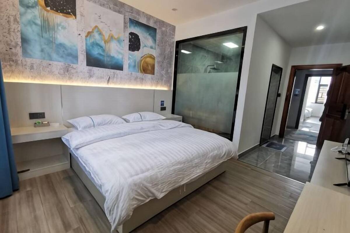 A modern hotel room with a large bed, a desk, and a bathroom with a glass shower.