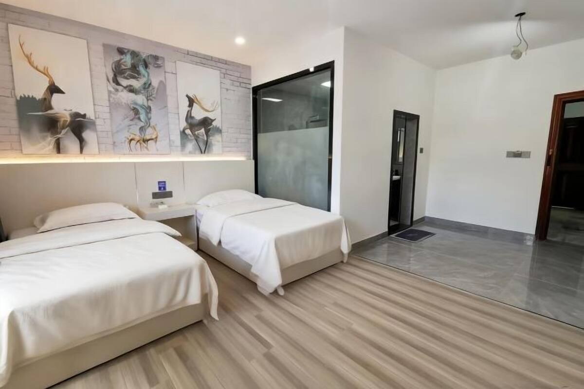 A hotel room with two beds, a wall-mounted artwork of deer, a large window, and a door.