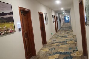 A hotel hallway with wooden doors, framed pictures on the walls, and a carpeted floor. - Ruili Chuan Hot Spring Hotel (Ruili)