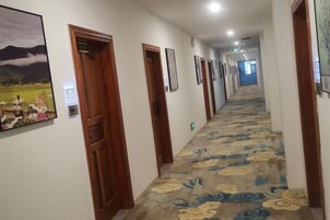 Un pasillo de hotel con puertas de madera, cuadros enmarcados en las paredes y suelo alfombrado.