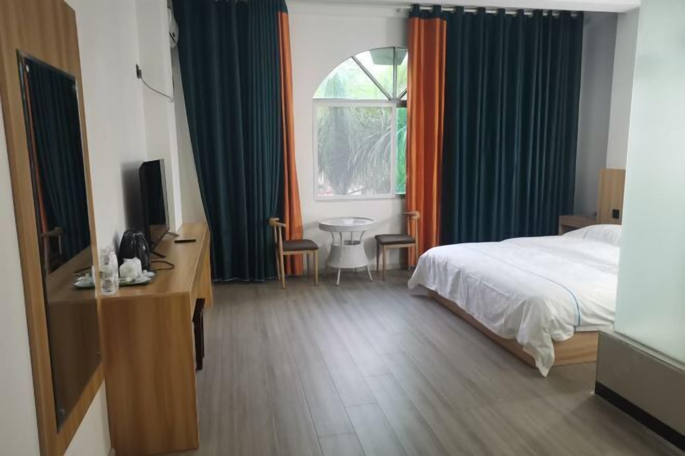 A hotel room with a bed, a desk with a chair, a small table with two chairs, and a window with curtains.