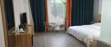 A hotel room with a bed, a desk with a chair, a small table with two chairs, and a window with curtains.