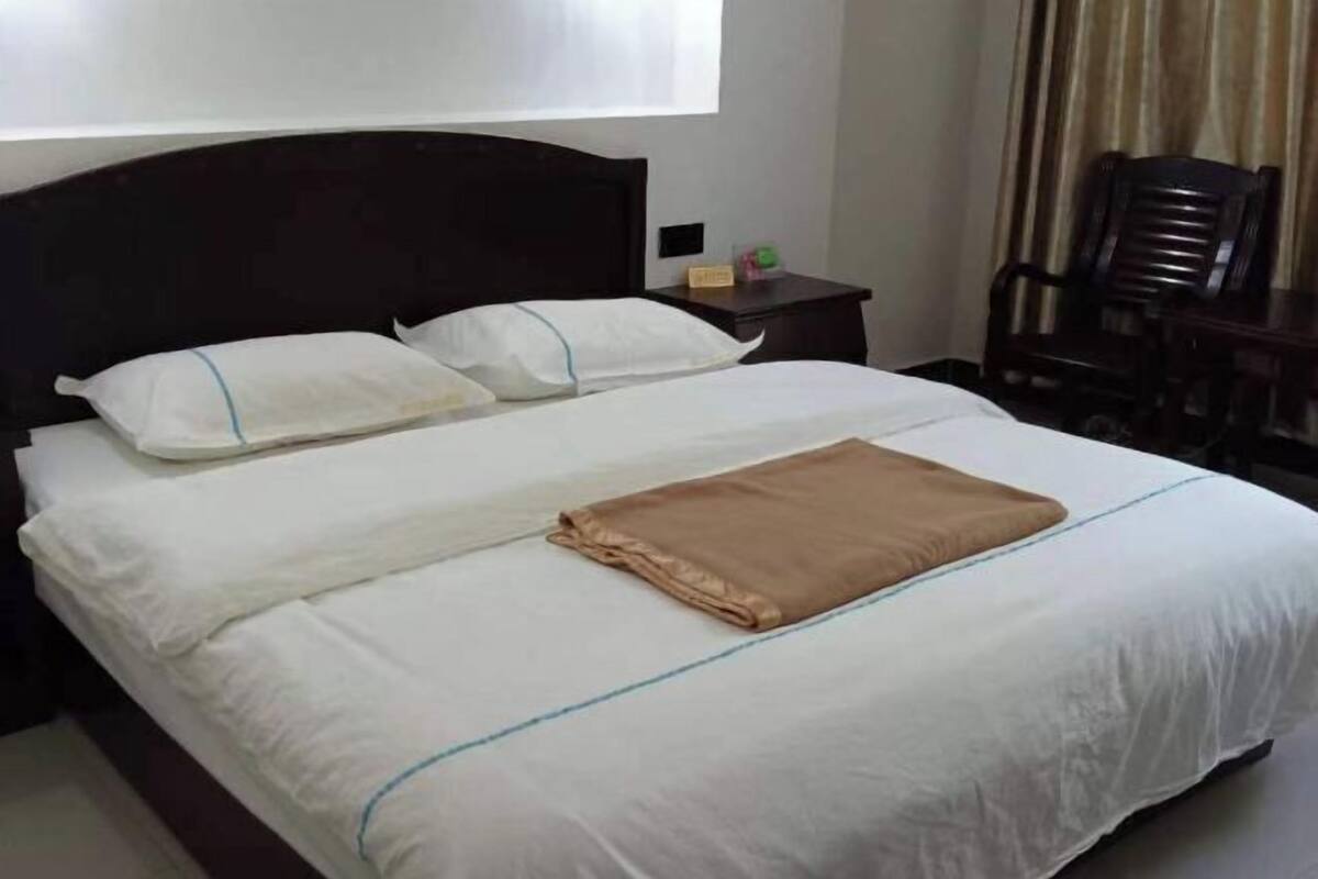 A neatly made bed with white linens and a brown blanket, a wooden headboard, a nightstand with a lamp, and a chair.