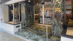 En hotellentrén med en fasad av marmor, glasdörrar och en trappa som leder upp till entrén.