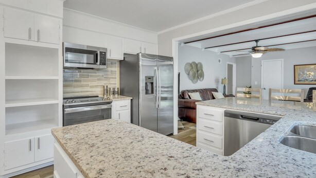 A modern kitchen with white cabinetry, stainless steel appliances, a granite countertop, and a built-in dishwasher.