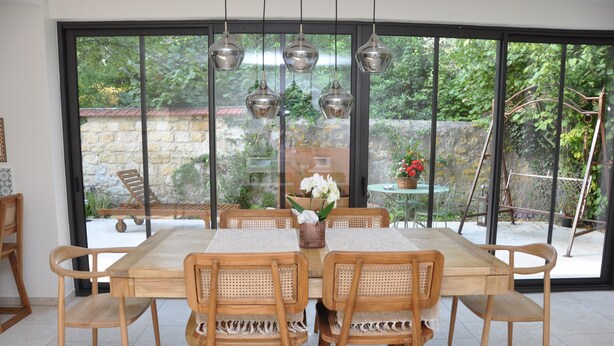 A dining area with a wooden table and chairs, large windows, and hanging pendant lights.