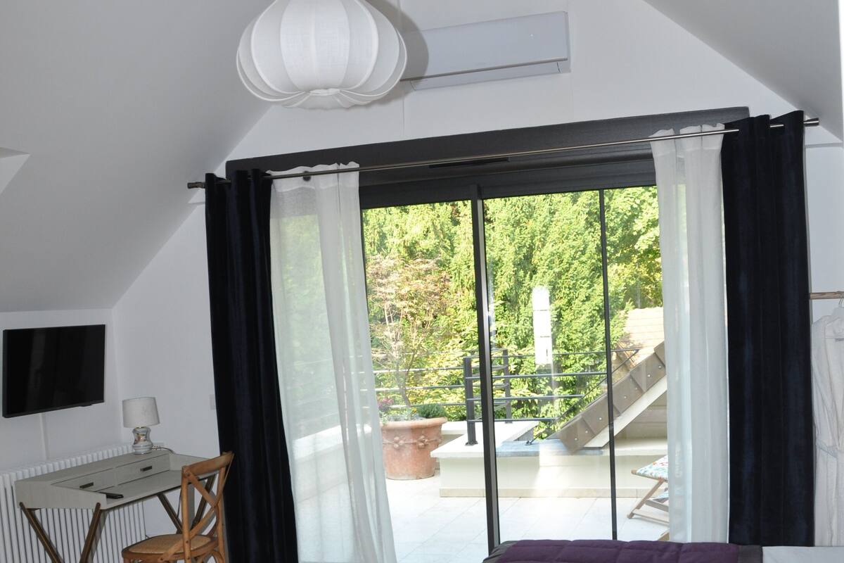 Une chambre à coucher avec un lit, un bureau et une chaise. Il y a une fenêtre avec des rideaux et une vue sur l’extérieur.