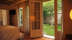 A room with a bed, a door leading to a garden, and a TV mounted on the wall.