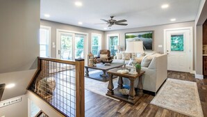 A spacious living room with a ceiling fan, a sofa, a coffee table, and a view of the outdoors through large windows.