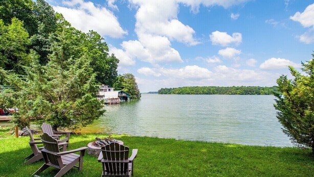 A lakeside view with a dock, chairs, and a building across the water.