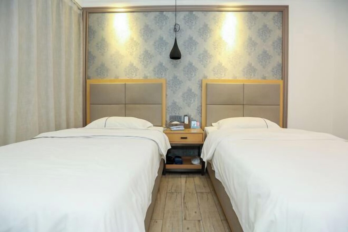 Een hotelkamer met twee eenpersoonsbedden, een houten nachtkastje ertussen, en behang met een patroon.
