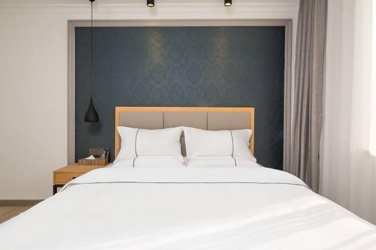 Uma cama bem arrumada com cabeceira de madeira, mesa de cabeceira com abajur e parede de cor escura.