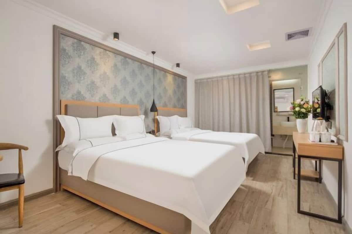 Quarto de hotel com duas camas, uma escrivaninha, uma cadeira e um espelho.