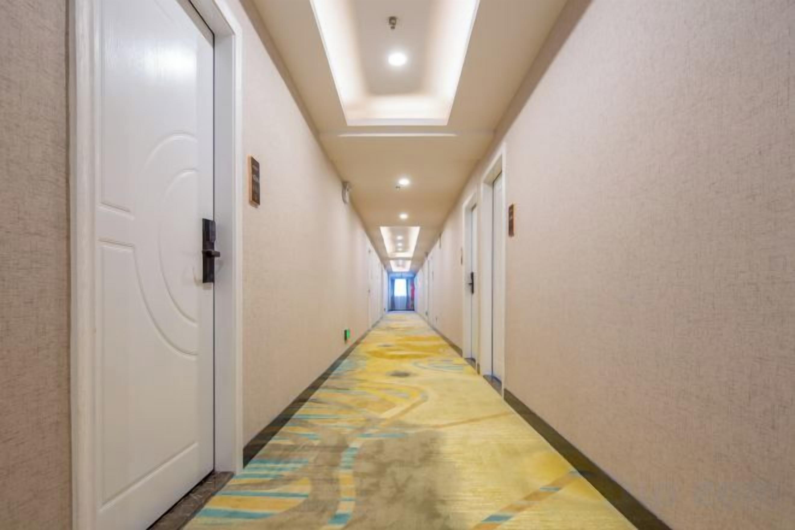 Un pasillo de hotel con puertas a ambos lados, una alfombra estampada e iluminación empotrada en el techo.