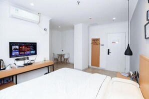 Een hotelkamer met een bed, een bureau met een computer, een televisie, een klein tafeltje en een deur.