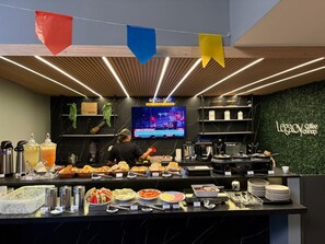 A buffet area with a variety of food items and a television displaying a news channel. - Melhores Flats - Charmoso perto do mar (João Pessoa)