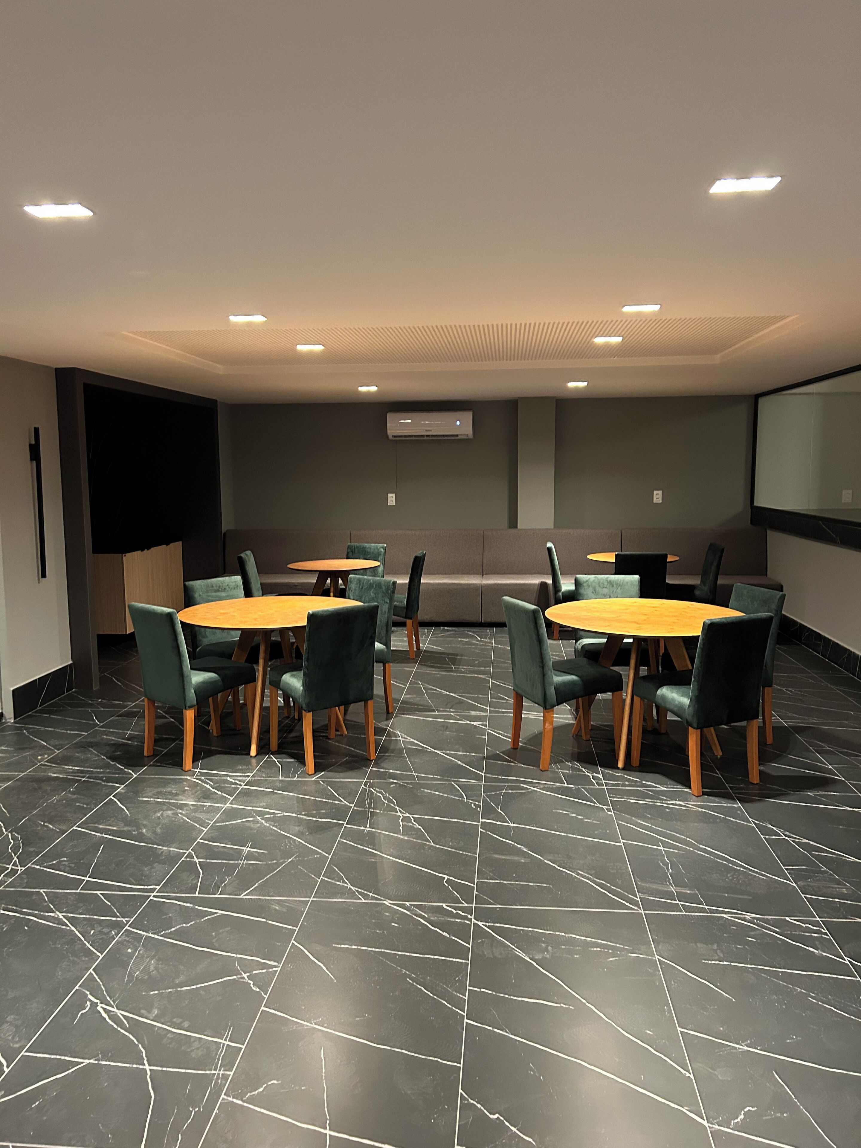 A conference room with two round tables, green upholstered chairs, a projector screen, and a wall-mounted air conditioning unit.