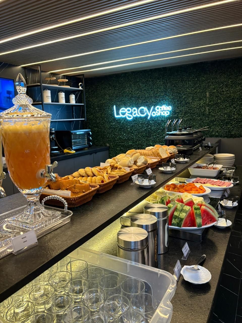 A buffet setup with various food items, a large punch bowl, and a neon sign reading "Legacy Coffee Shop".